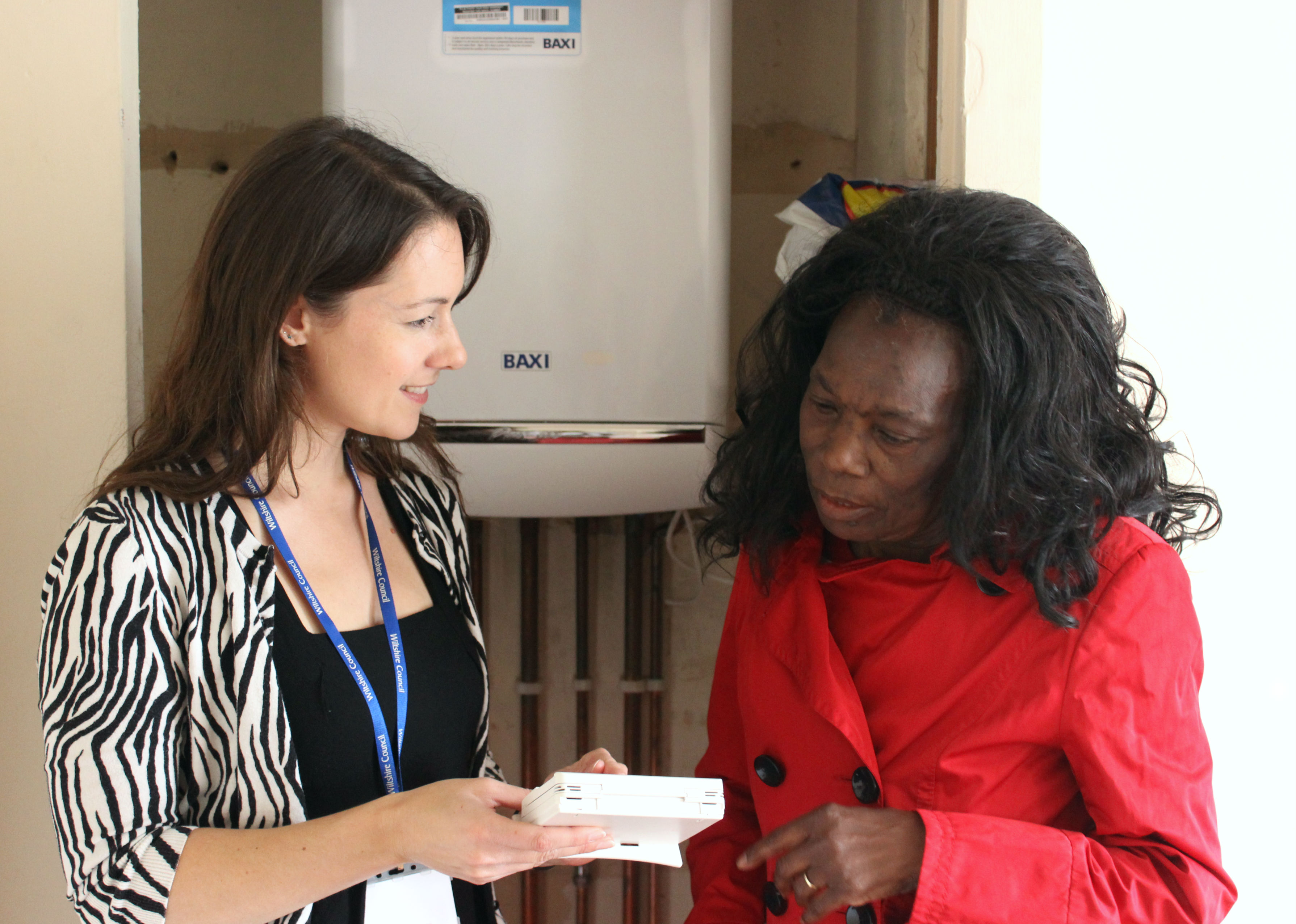 Two women looking at a device and stood in front of a boiler