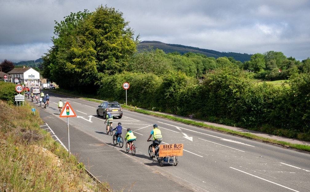 A group of cyclists cycling along a road into Bamford village as part of a bike bus for students