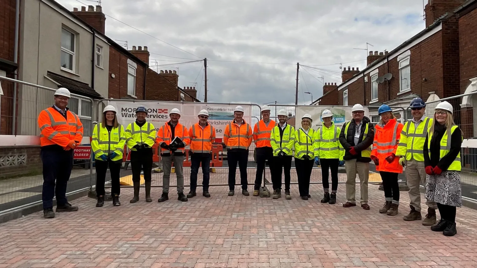 A group of people in high viz jackets and hardhats stand on the newly laid permeable street paving