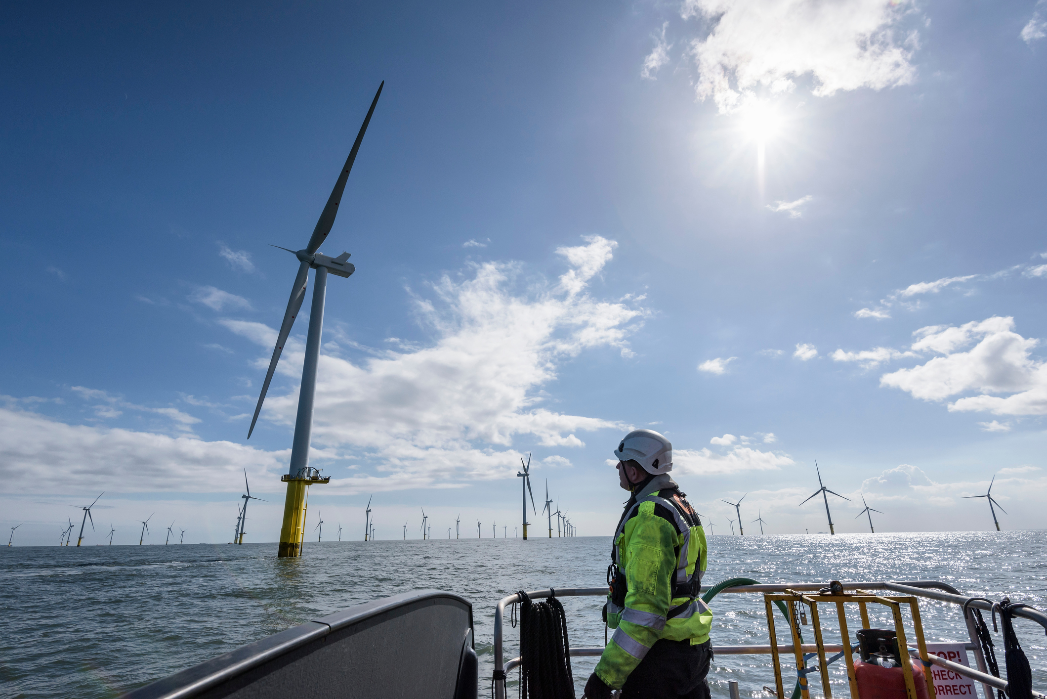 Man in hi-vis jacket stands on a platform looking at offshore wind farms