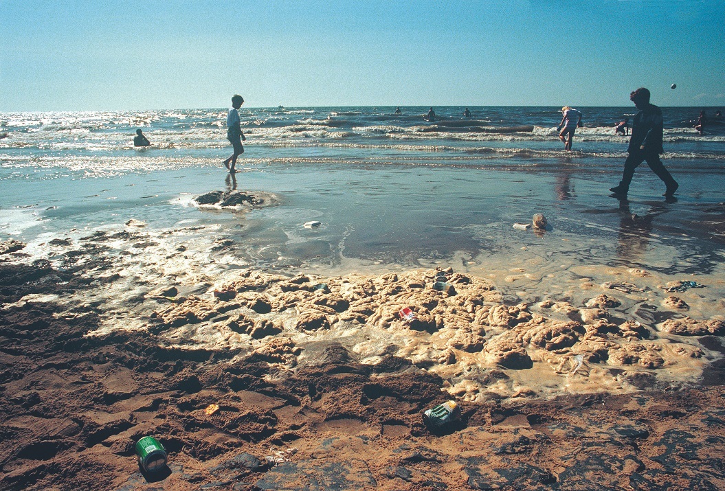 People paddling with sewage and foam on the shoreline