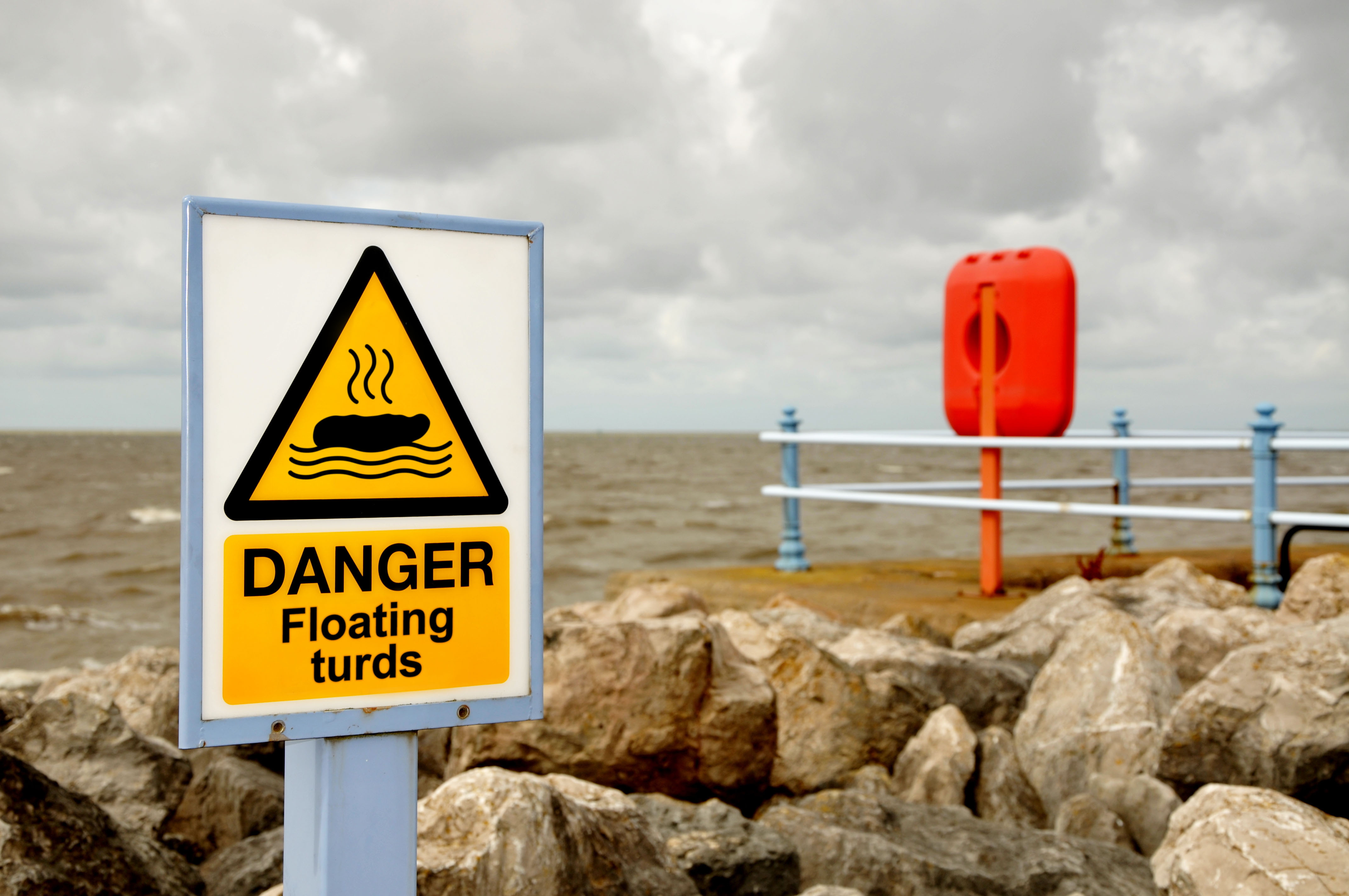 Floating turds warning sign in front of a cloudy beach