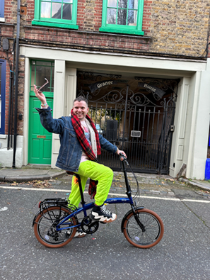 A man posing on a bike on the street, with his arm raised in celebration