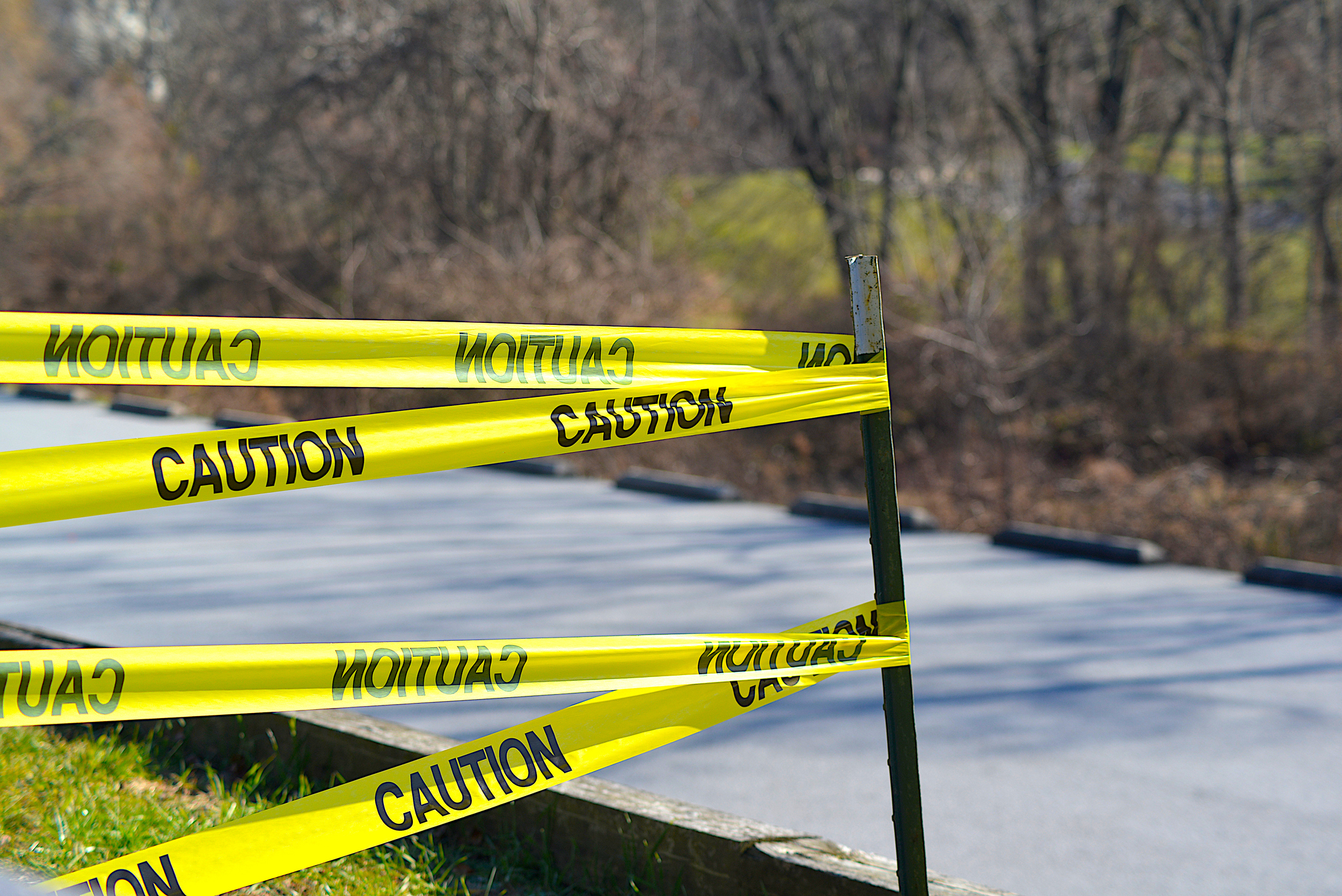 Yellow and black tape reading "caution" with a backdrop of a road and trees