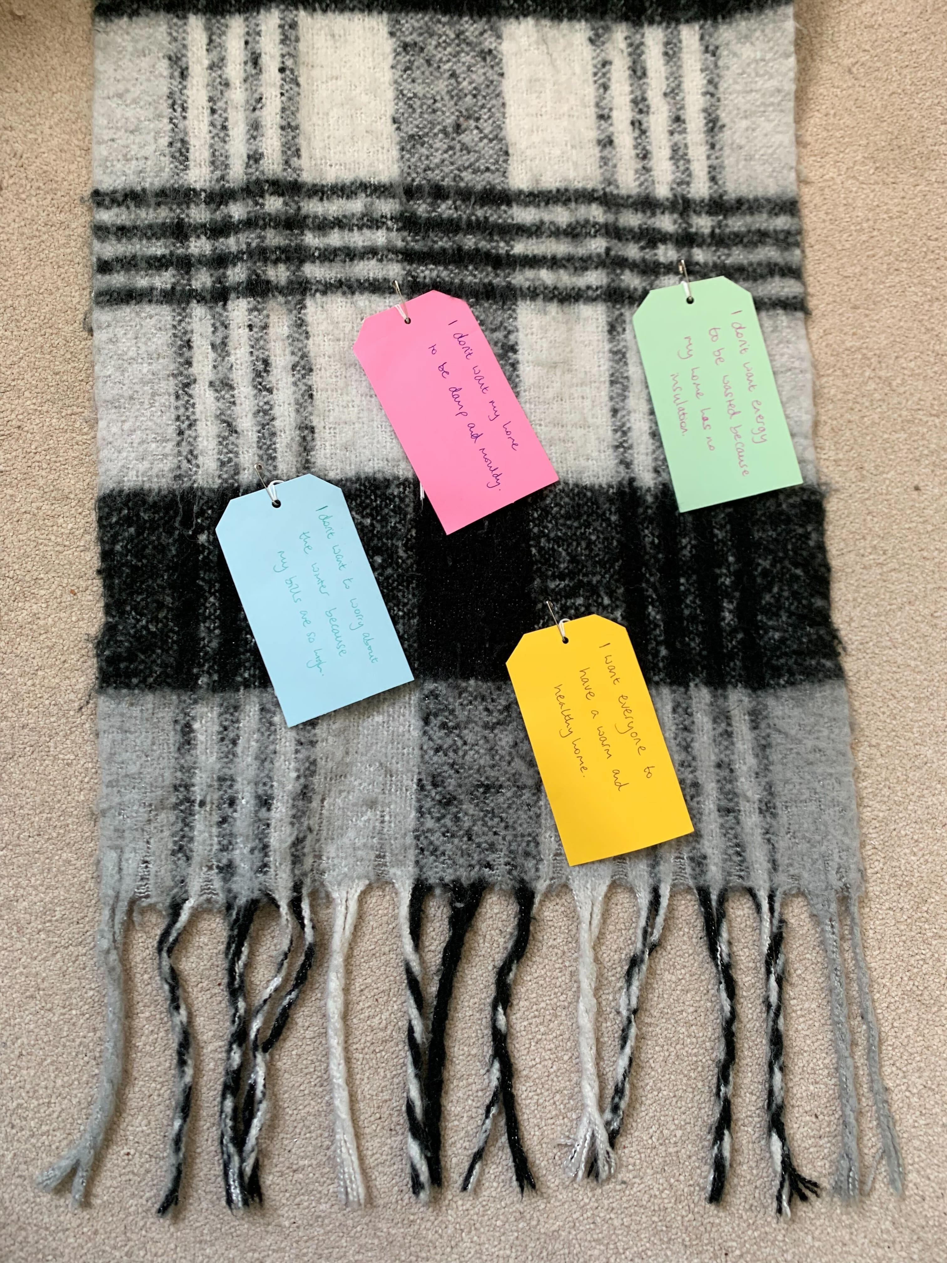 A black and white checked scarf with colourful paper tags attached to it. The tags have handwritten messages on them.