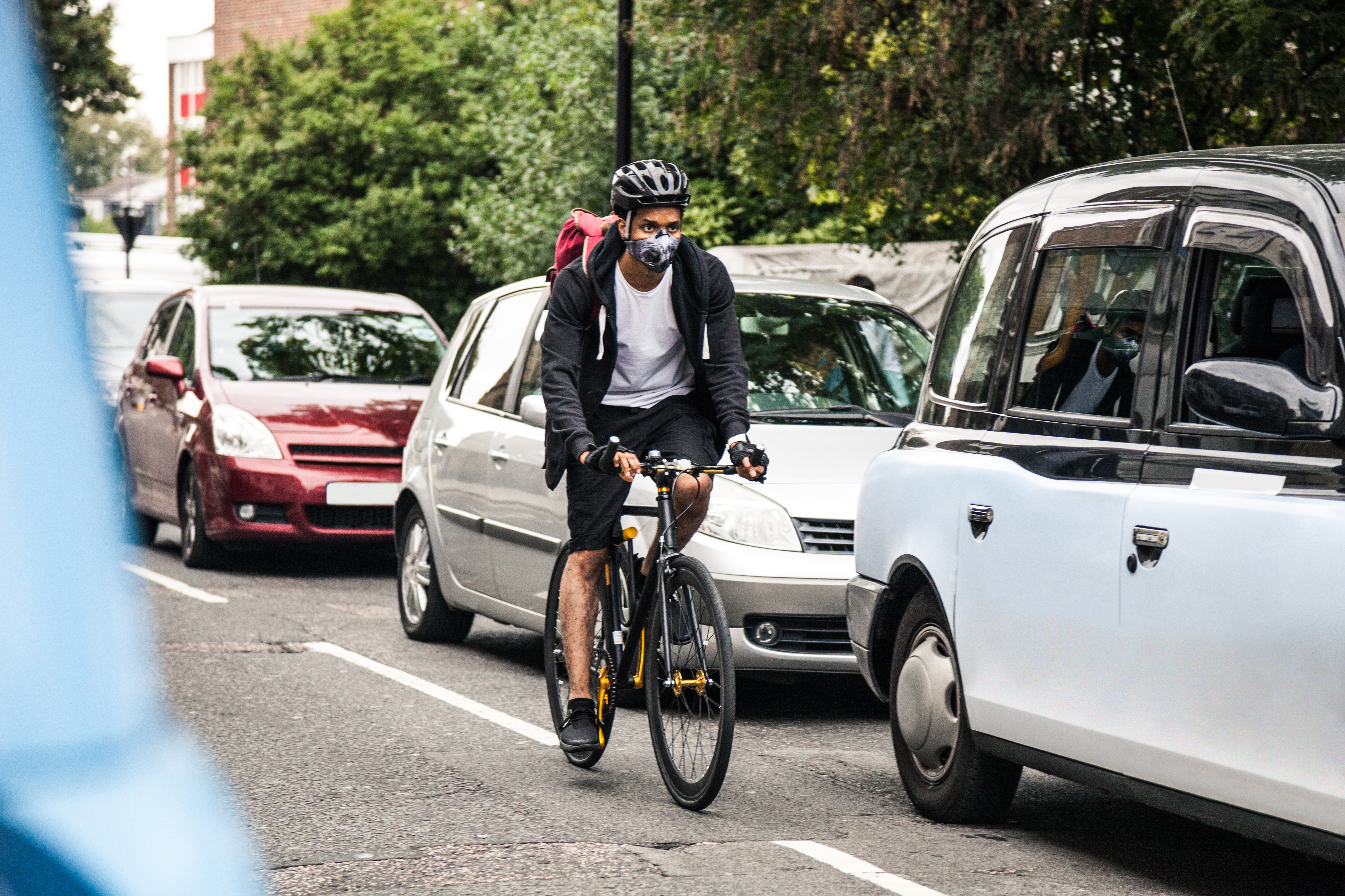 Air pollution Cyclist commuter wearing a pollution mask in Central London while cycling alongside several cars