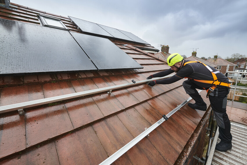 Home solar panels A worker installing solar panels onto a tiled roof