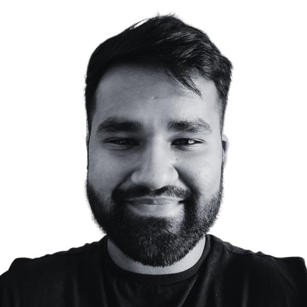 A south Asian man smiling. He looks friendly. The photo is a passport style headshot in black and white.