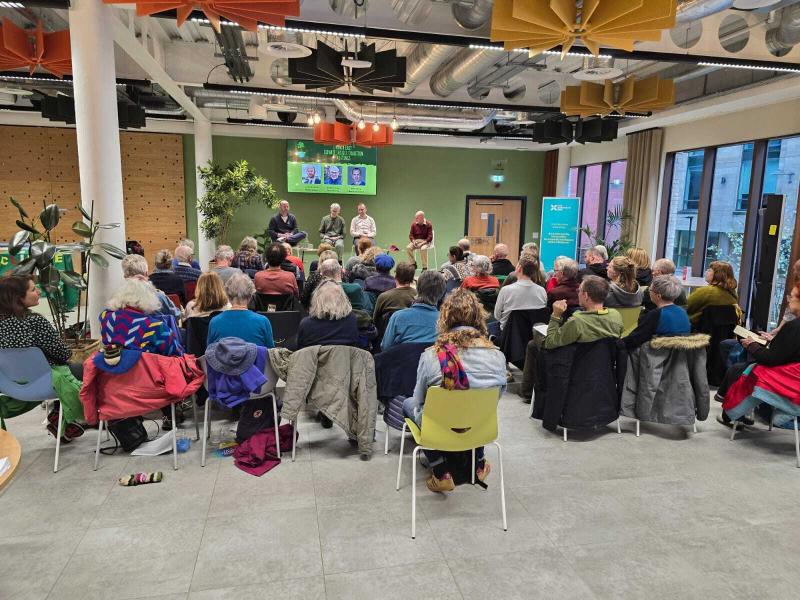 Audience members sat watching 4 panellists talk on a stage