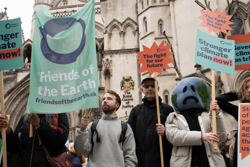 A group of people stood outside the Royal Courts of Justice with banners demanding a stronger climate plan, now.