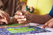 Close-up of a person's hands as they stitch the square of a quilt