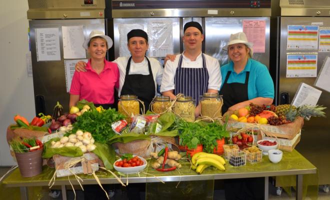 Four chefs stand in front of a table full of colourful fruit and vegetables.