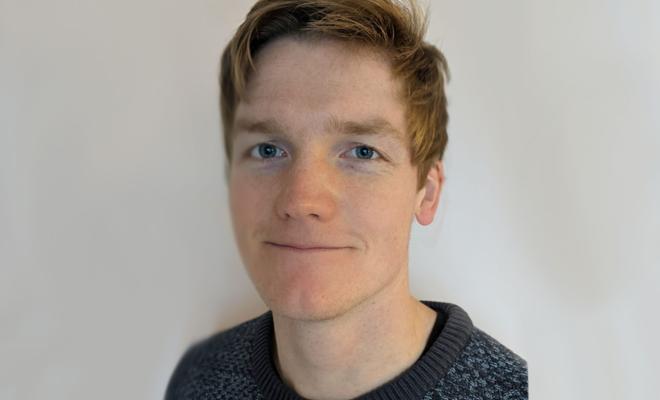 A headshot of a young man with ginger hair smiling and looking straight on.