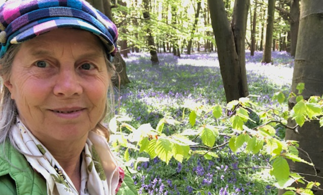 A selfie of a woman in beautiful woods, wearing a bright jacket and a colourful hat.
