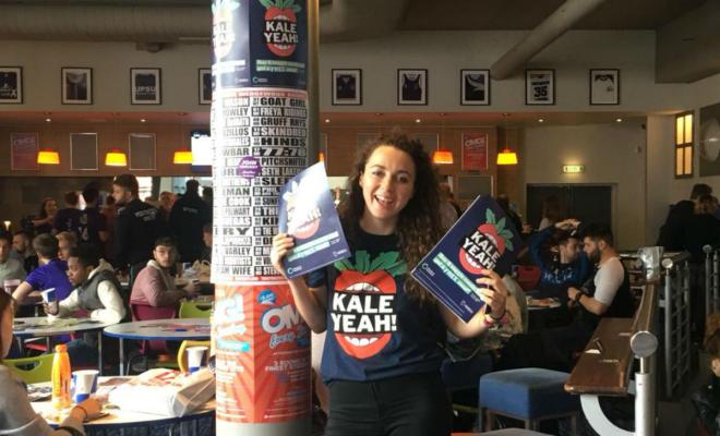 Student ambassador in bar holding Kale Yeah! promotional materials