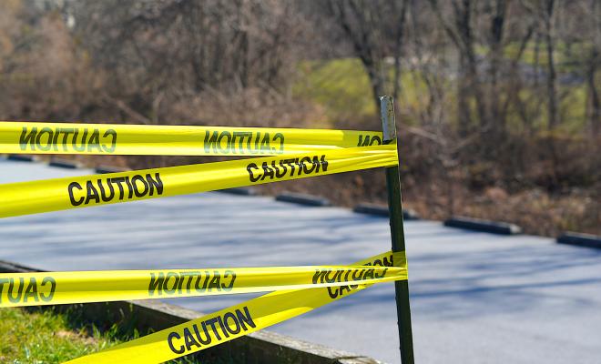 Yellow and black tape reading "caution" with a backdrop of a road and trees