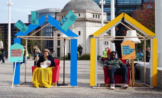 Two model houses with one person sat inside each. One is blue, is leaking money and the person is wrapped up in blankets. The other is yellow and the person looks warm.