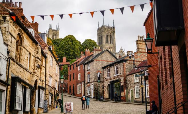 A cobbled street lined with houses and shops, and a cathedral in the distance